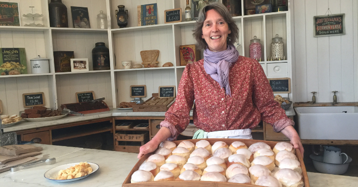 woman smiling at the camera holding a tray of frshly baked iced buns at the Edwardian Bakery Beamish Museum.